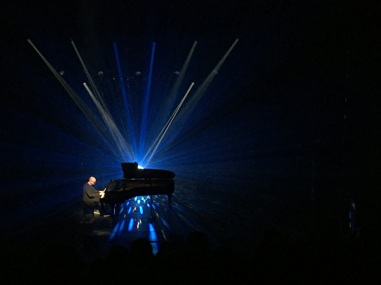 Un pianiste joue sur un piano à queue sur une scène sombre.