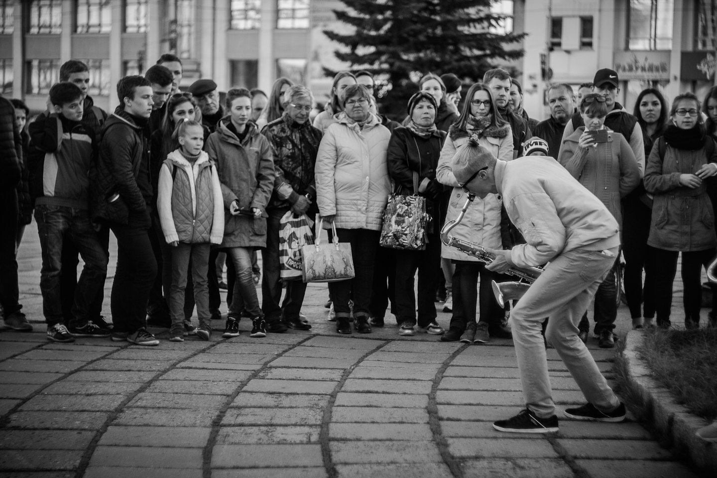 Musicien de rue jouant du saxophone devant une foule sur un trottoir.