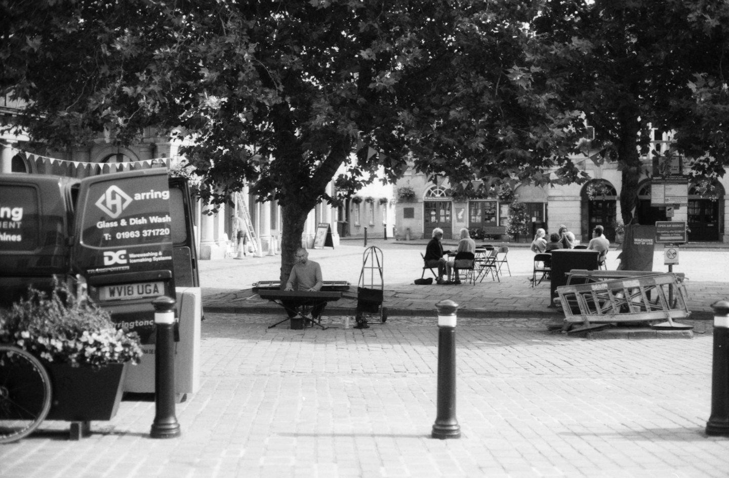Un musicien joue du clavier sous un arbre sur une place de ville animée.